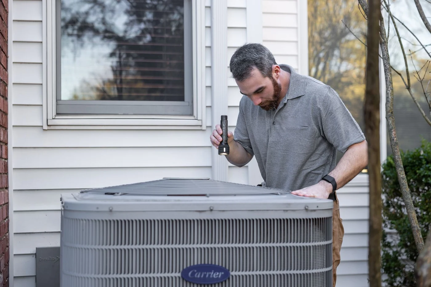 Technician inspecting an outdoor condenser unit with a flashlight